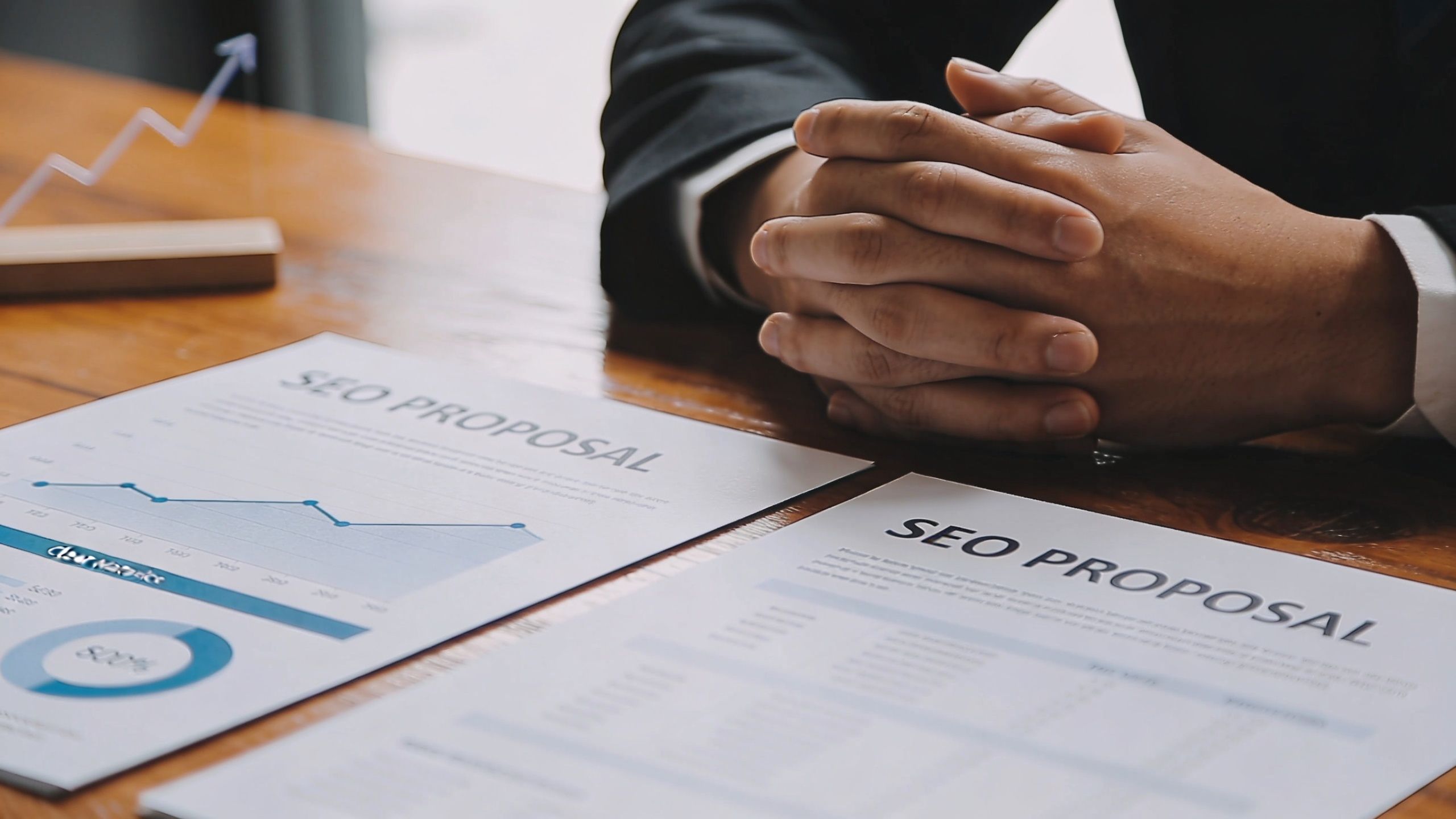 A professional in a suit reviewing SEO proposal documents and data charts at a wooden desk.